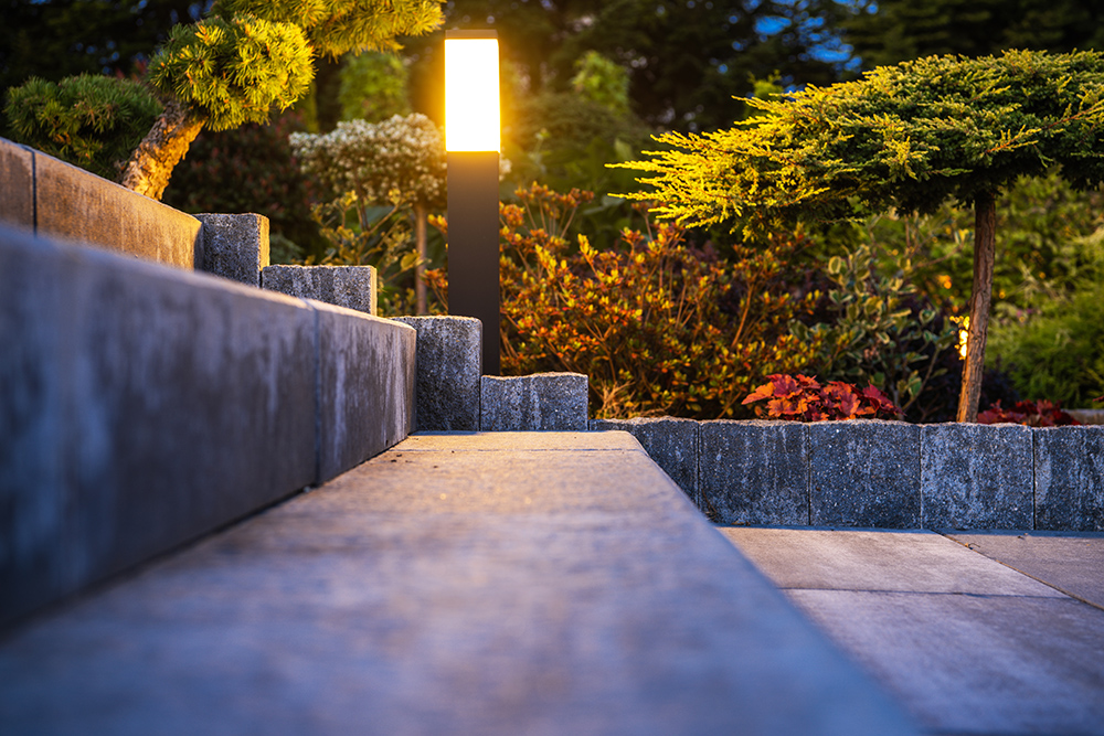Outdoor Garden Light Installed Along Concrete Backyard Stairs Lighting Them Up in the Evening. Landscaped Garden in the Background.